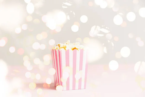 Bolsa de palomitas de maíz con rayas blancas y rosadas en el telón de fondo festivo luces bokeh. Fondo minimalista vacío. Noche romántica de cine y concepto de snack —  Fotos de Stock