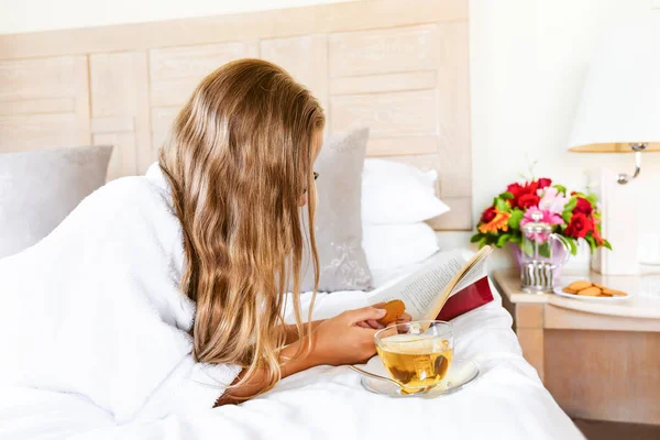 Menina relaxante em seu quarto de hotel: lendo com um copo de bebida espumante. Conceitos de férias, relaxamento, auto-tempo e fuga — Fotografia de Stock