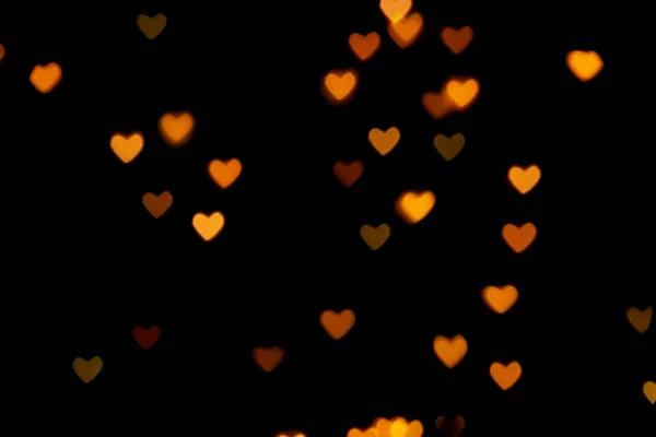 Black background with bright warm heart shaped bokeh lights. Holiday, Valentines Day background. Ideal to layer with any design