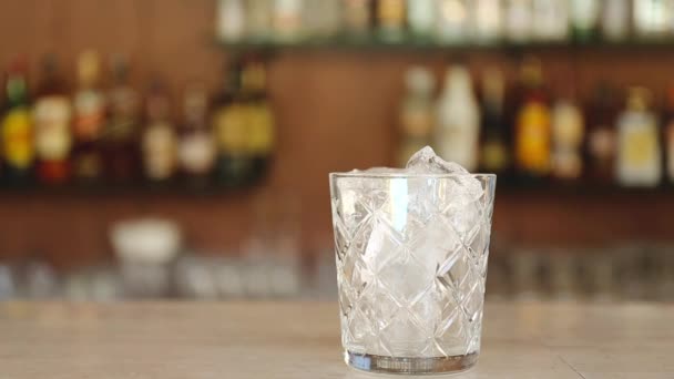 Стакан вкусного алкогольного коктейля негрони с апельсиновым ломтиком на барной стойке. Наливание коктейля в стакан — стоковое видео