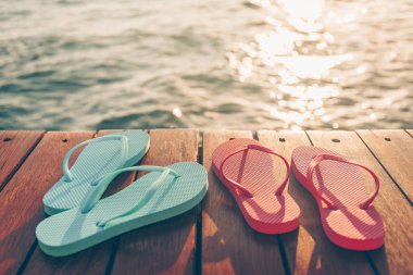 Gün batımında tahta iskelede iki çift parmak arası terlik. Lüks tatil köyü. Tatil kaçamağı kavramı