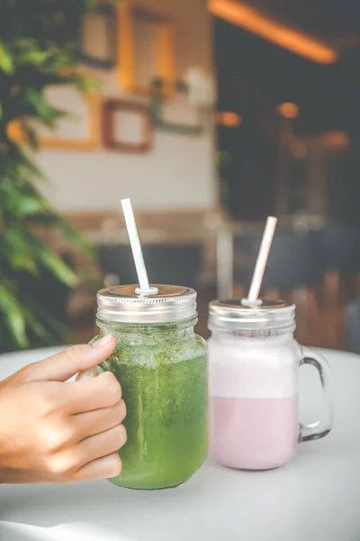 Woman hand holding healthy smoothie in eco friendly glass jar with paper straws in a luxury gym recreation area or vegan cafe