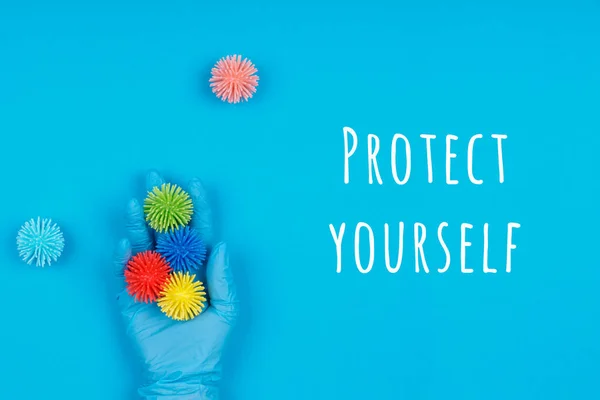 Hand in Hand Einweghandschuh mit Plastikbällen auf blauem Hintergrund mit der Aufschrift "Protect yourself". Epidemische, saisonale Viren, soziale Isolation, Abschaltung, Coronavirus COVID-19-Konzept — Stockfoto