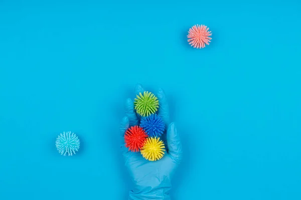 Mano en guante desechable con virus de bolas de plástico en el fondo azul. Epidemia, virus estacionales, aislamiento social, parada, coronavirus COVID-19 concepto — Foto de Stock