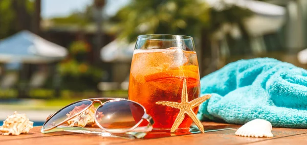 Glass of aperol spritz or negroni cocktail with seashells, towel and sunglasses