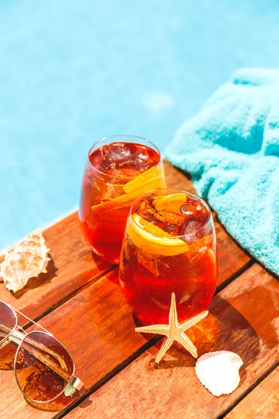 Twee glazen aperol spritz en negroni cocktail met schelpen, handdoek en zonnebril. Stockafbeelding