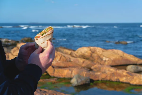 El hombre está comiendo comida para llevar en la aislada playa rocosa del océano. —  Fotos de Stock