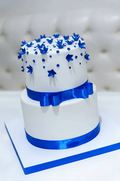White wedding cake with blue flowers and a bow. — Stock Photo, Image