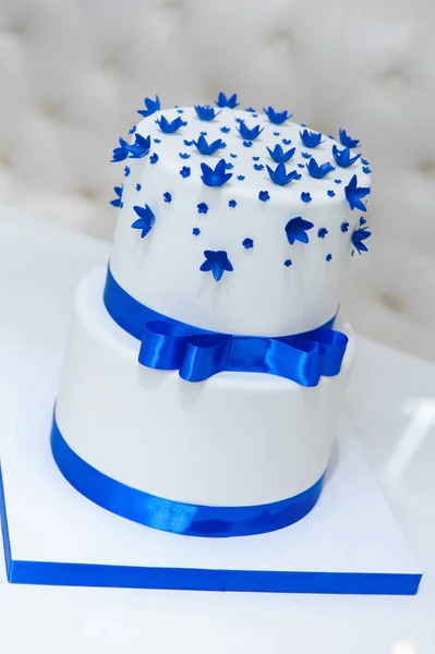 White wedding cake with blue flowers and a bow. — Stock Photo, Image