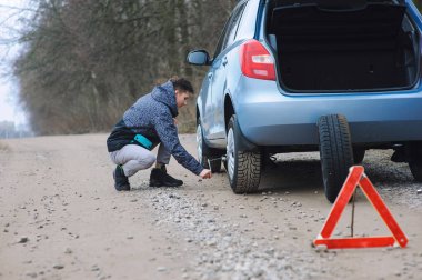 Adam arabanın lastiğini değiştiriyor.