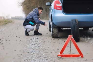 Adam arabanın lastiğini değiştiriyor.