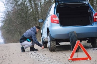 Adam arabanın lastiğini değiştiriyor.