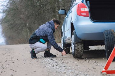 Adam arabanın lastiğini değiştiriyor.