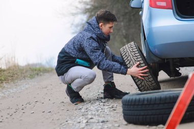 Adam arabanın lastiğini değiştiriyor.