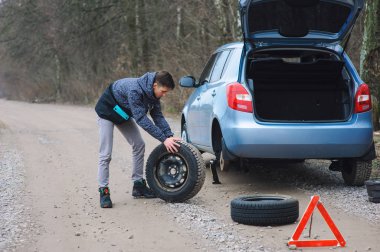 Adam arabanın lastiğini değiştiriyor.