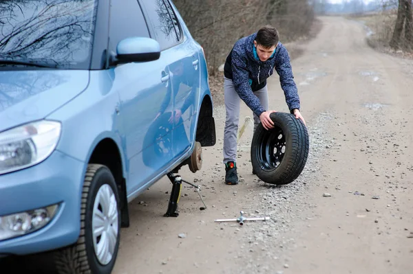 A man broke a wheel on a car and changes it on his own on the ro