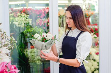 Bir çiçekçinin sahibi beyaz güllerden bir buket yapar.