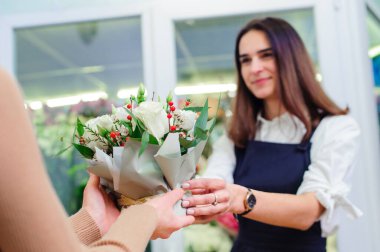Çiçek dükkanı sahibi alıcıya bir buket beyaz gül satar.