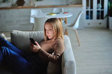 Akşamları evde kanepede uzanan kadınlar akıllı telefon kullanır.