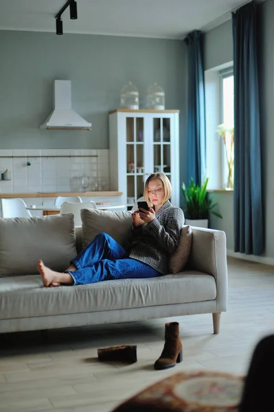 ソファに横になりながら自宅で夕方のスマートフォンの女性の使用 — ストック写真