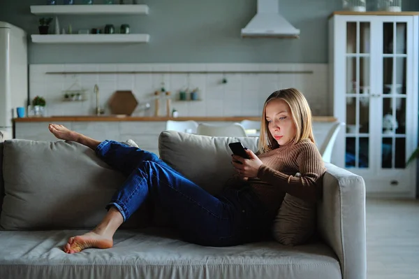 Woman use of smartphone in the evening at home while laying on sofa