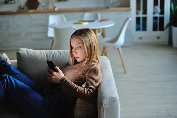 Woman use of smartphone in the evening at home while laying on sofa