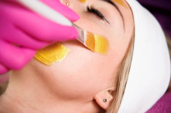 化妆品面具 美容师给女人的脸戴上金色的面具 在美容院接受面部治疗的美女 — 图库照片