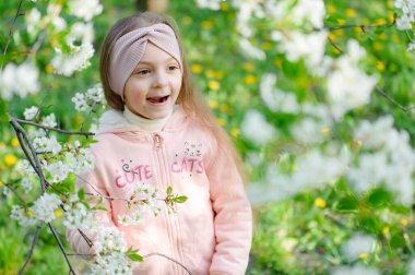 Çiçek açan kiraz ağacının yanında küçük güzel bir kız portresi. Yeşil arka planda gülümseyen çocuk