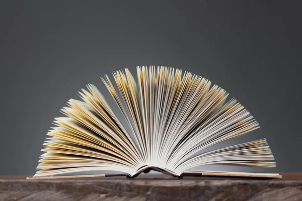 Aufgeschlagenes Buch bildet einen Fächer auf einem Holztisch — Stockfoto
