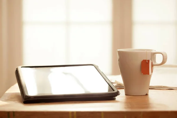 Moderna digitala enheter på träbord, suddig windows bakgrund, Digital tablett, te och tidningen — Stockfoto