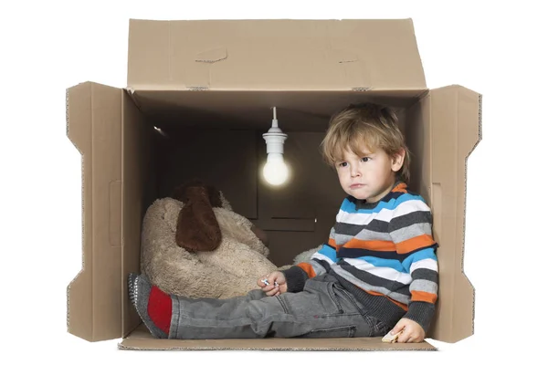 かわいい幼児男児で段ボール箱に裸電球、窮屈な小さな場所を表す彼のぬいぐるみのおもちゃ — ストック写真