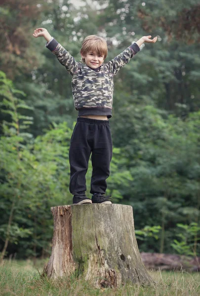 Χαριτωμένο μικρό αγόρι στέκεται σε έναν κορμό δέντρου χαρακτήρα: αναπτύσσονται όπου μπορείτε φυτεύονται έννοια — Φωτογραφία Αρχείου