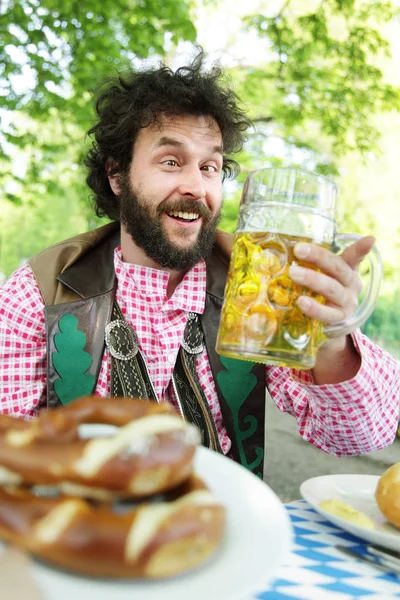 Ein bayerischer Bärtiger im Biergarten sagt Prost! Prost! mit Bierkrug oder Glas und Brezel — Stockfoto