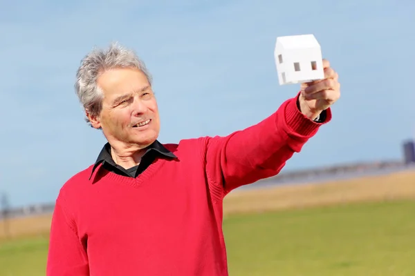 Serie di un pensionato anziano felice, immaginando la sua nuova casa futura con una piccola casa di carta — Foto Stock