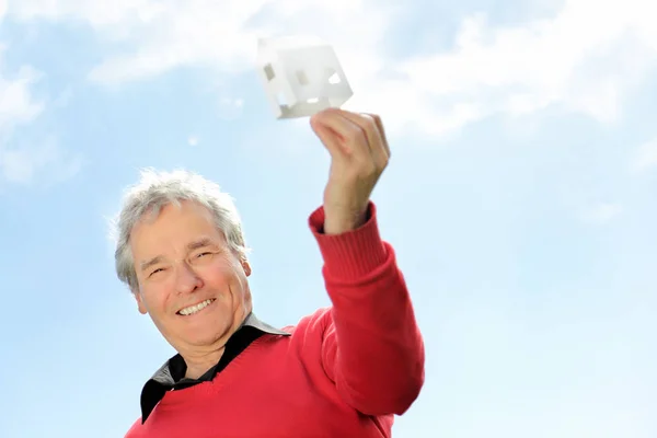 Serie di un pensionato anziano felice, immaginando la sua nuova casa futura con una piccola casa di carta — Foto Stock