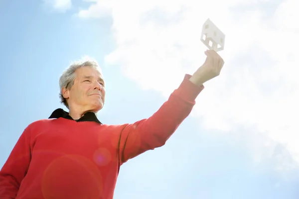 Serie di un pensionato anziano felice, immaginando la sua nuova casa futura con una piccola casa di carta — Foto Stock