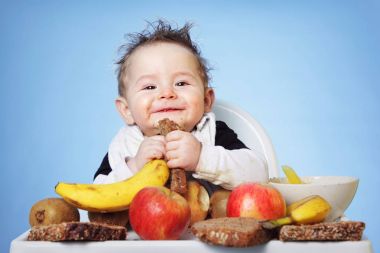 Cute Baby boy eating healthy food for breakfast on bright blue background: horizontal clipart