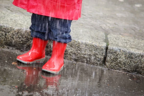 Μικρό αγόρι με κόκκινο βροχή ρούχα διασκέδαση σε λακκούβες έξω σε έναν δρόμο στο Βερολίνο — Φωτογραφία Αρχείου