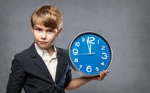 Poważne 7-letniego chłopca, trzymając niebieski duży zegar, zaledwie kilka minut przed północą: albo, on ostrzega nas, że czas jest na wyczerpaniu, lub gotowy do świętowania nowego roku — Zdjęcie stockowe