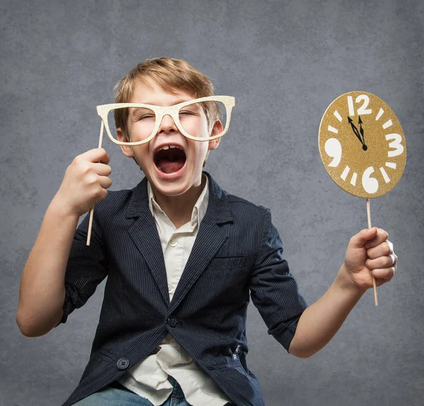 Gelukkig Nieuwjaar-serie, met een 7-jarig olf gelukkige houdt jongen, meerdere Photo Booth Items, terwijl je plezier. Met klok minuten voor middernacht tegen grijs beton achtergrond — Stockfoto