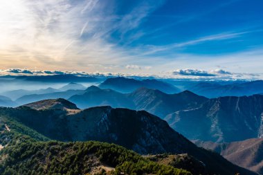 Beautiful captivating landscape of the layered misty hazy French Alps mountain range in Alpes-Maritimes in the afternoon during a sunny day