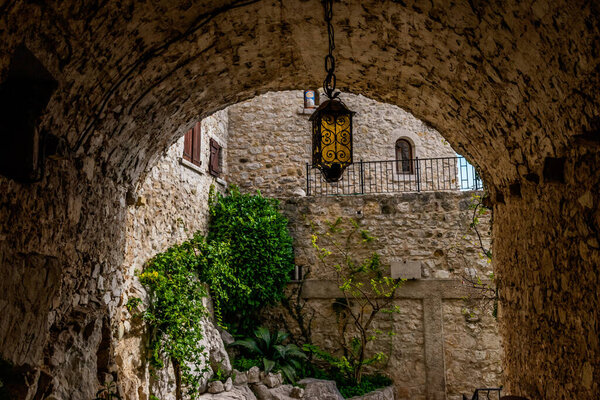 A tunnel-like passage of an old medieval town with a crafty metal lantern hanging in the middle (Eze old town, Cote d'Azur, France)