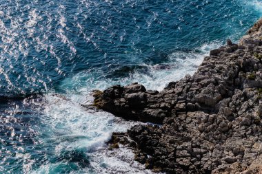 Akdeniz turkuaz suyu ve kıyıdaki kayalara vuran güçlü dalgaların yakın plan çekimi.