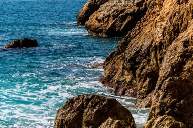 Akdeniz turkuaz suyu ve kıyıdaki kayalara vuran güçlü dalgaların yakın plan çekimi.