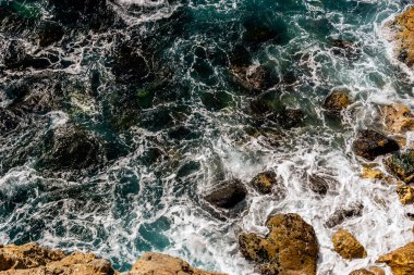 Akdeniz turkuaz suyu ve kıyıdaki kayalara vuran güçlü dalgaların yakın plan çekimi.