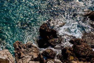 Akdeniz turkuaz suyu ve kıyıdaki kayalara vuran güçlü dalgaların yakın plan çekimi.