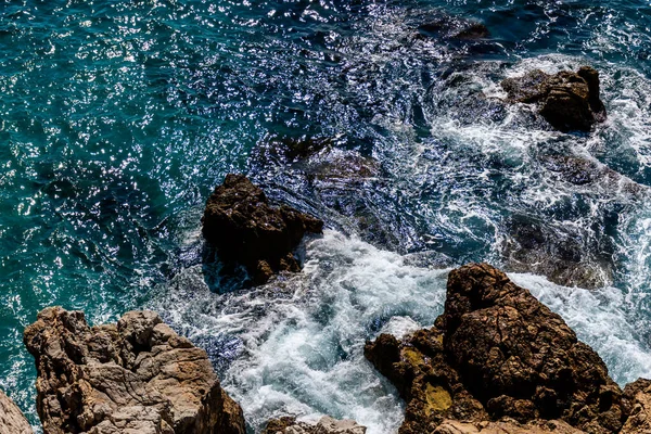 地中海の終わりのショットターコイズブルーの水と海岸の岩に対して打つ強力な波 — ストック写真