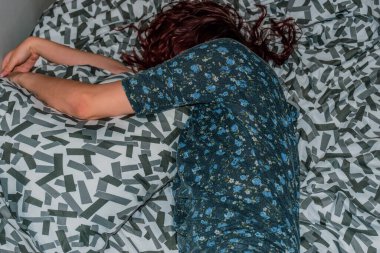 Yastığın yanındaki yatakta yatan, tanınmayan, beyaz saçlı, genç bir kadının yakın plan fotoğrafı.