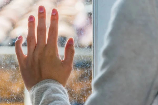 A close-up shot of a young Caucasian female hand on the window glass with the old French apartment building\'s rooftop in the background