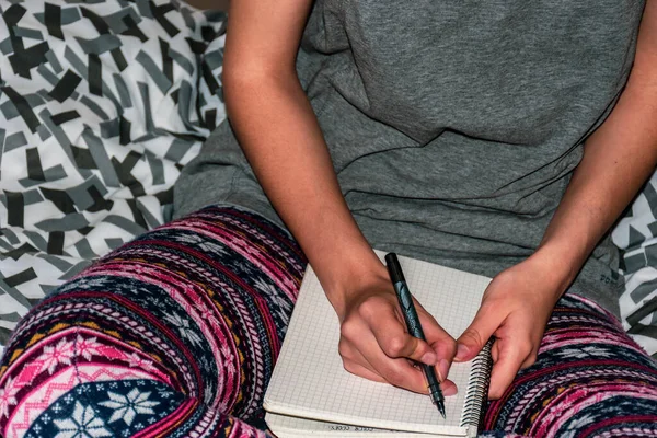 ベッドの上に座りノートを膝の上に置き何かを書き留めています — ストック写真